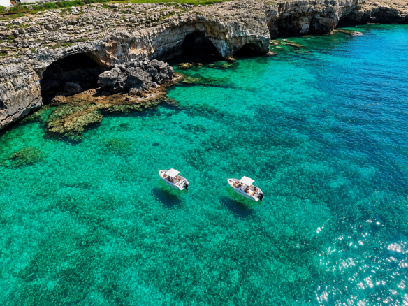 Barche davanti alle grotte marine del Salento con mare turchese e scogliere della Puglia.
