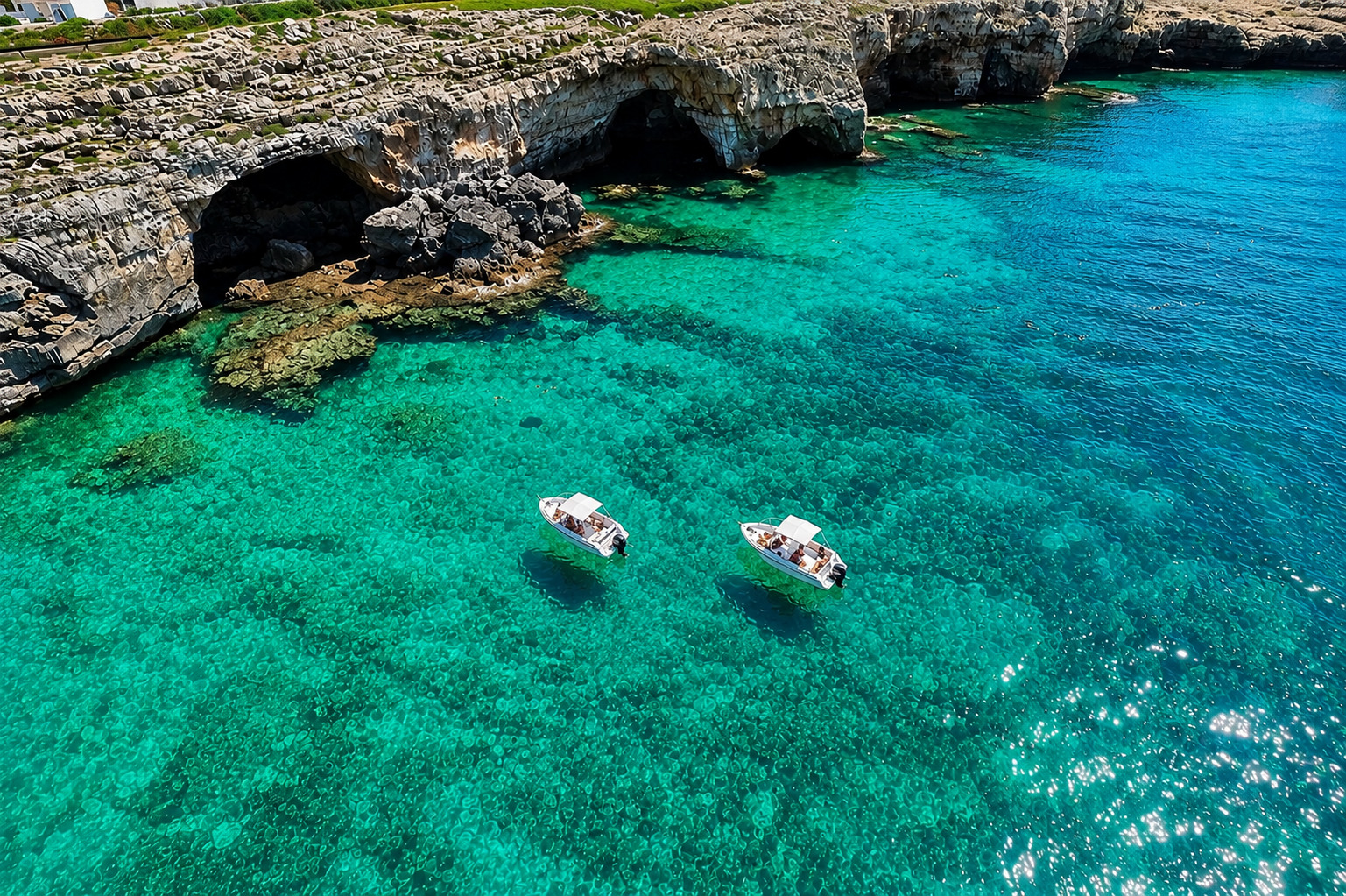 Barche davanti alle grotte marine del Salento con mare turchese e scogliere della Puglia.